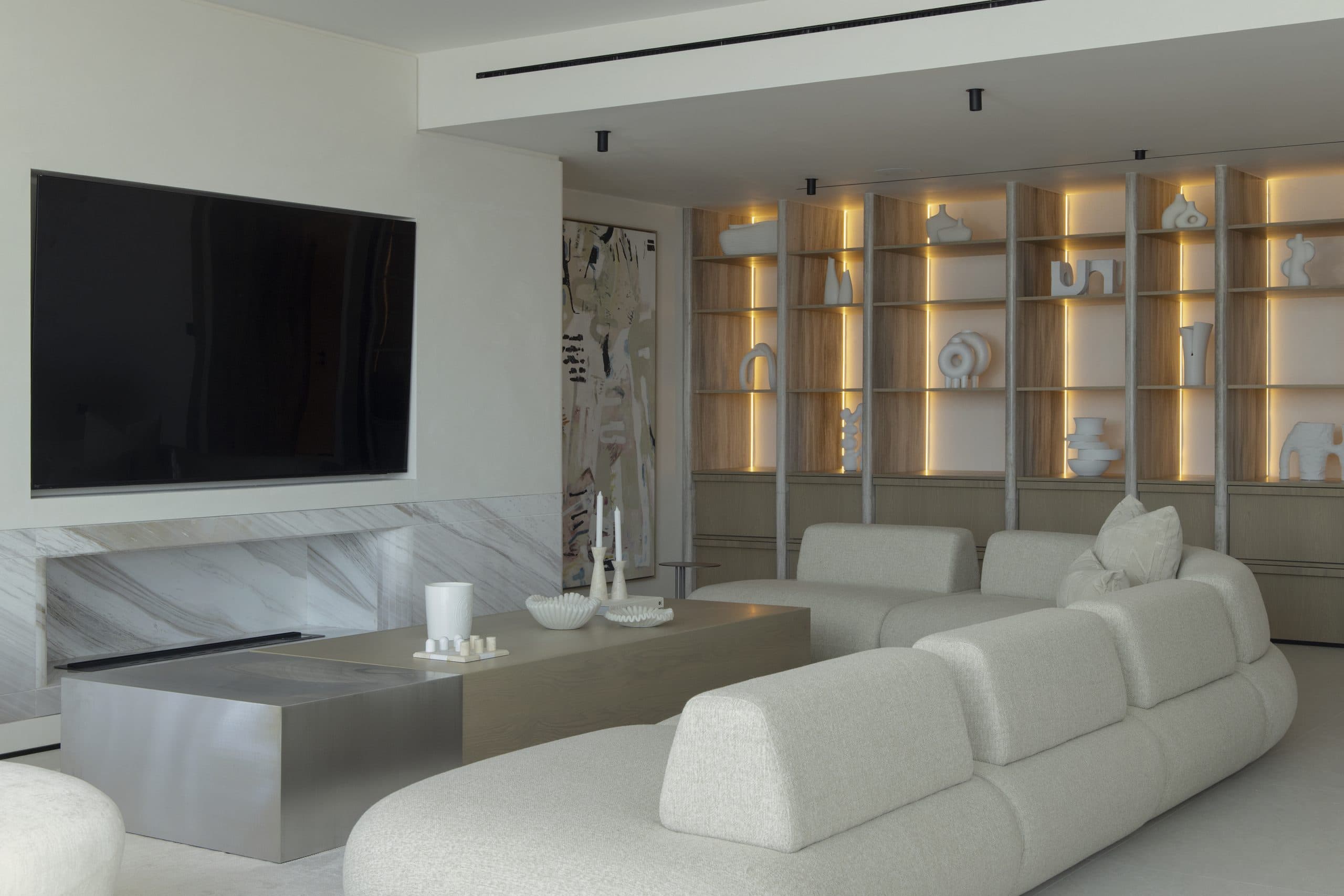 Full-height oak shelving wall with integrated lighting beside a marble-clad media wall
